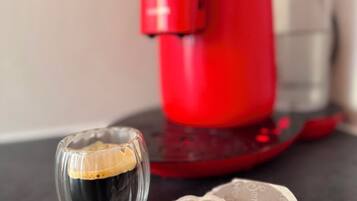 Una cafetera roja, una taza de vidrio con café y dos posavasos con texto.