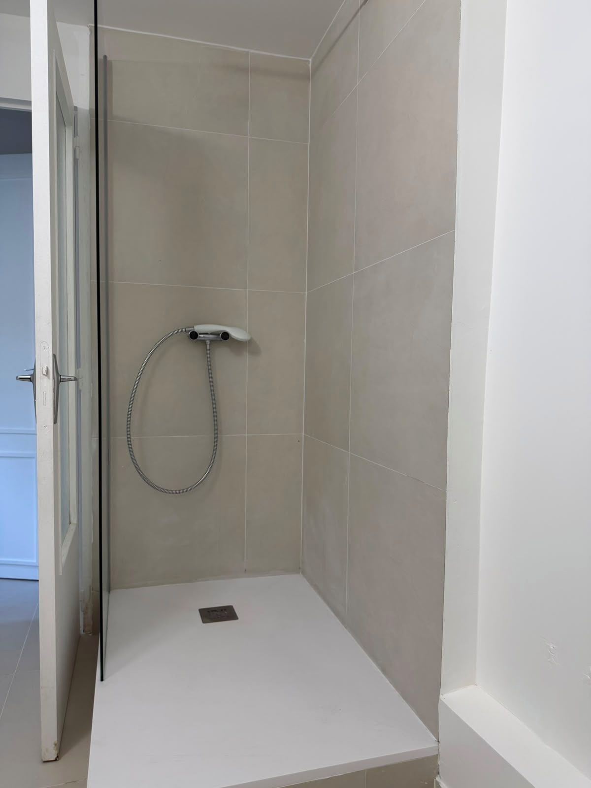 A small, enclosed shower area with a handheld showerhead and a drain.