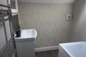 A bathroom with a white sink, a mirror, a towel rack, and a shower area. - The Trafalgar (Scarborough)