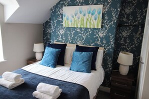 A bedroom with a bed, pillows, a painting, and a nightstand. - The Trafalgar (Scarborough)