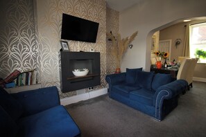 A living room with a fireplace, blue sofas, a flat-screen TV, and a bookshelf. - The Trafalgar (Scarborough)