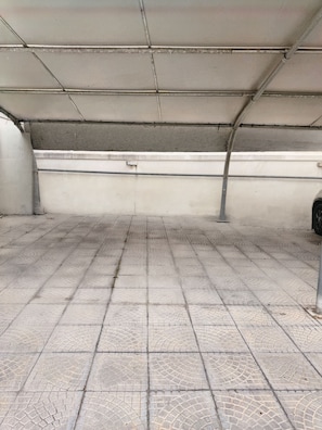 Ein mit Fliesen ausgelegter Boden mit Gittermuster, eine weiße Wand mit einer Metallrohrleitung und eine Decke mit einer Rasterstruktur.