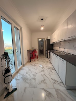 Una cocina moderna con piso de mármol, una zona de comedor con sillas rojas y vistas por la puerta de vidrio.