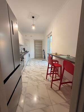Eine Küche mit Kühlschrank, Spüle und einer Essecke mit roten Stühlen.