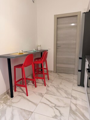 Una cocina con piso de mármol, encimera gris, dos sillas rojas y una puerta cerrada.