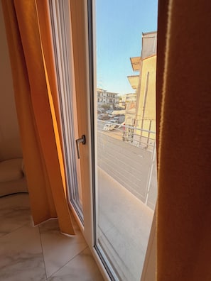 Ein Zimmer mit großem Fenster, einer Tür und Blick auf eine Straße mit Gebäuden und parkenden Autos.