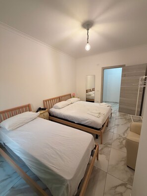 Habitación de hotel con dos camas, una mesita de noche, una lámpara, un espejo y la puerta del baño.