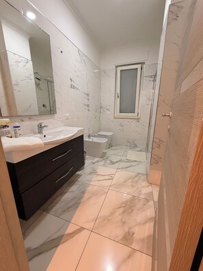 Un baño con piso de mármol, tocador con lavamanos, espejo y retrete.