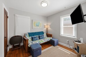 Ein gemütliches Wohnzimmer mit einer Couch, Hocker, einer Lampe und einem an der Wand befestigten Fernseher.