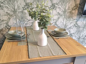 A dining table with a vase of green foliage, two wine glasses, and a set of plates and bowls. - Old Coach House Apartment (Scarborough)