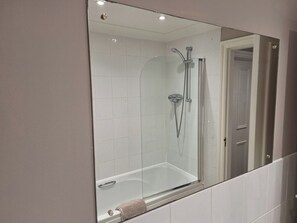 A bathroom with a glass-enclosed shower, white tiles, and a large mirror. - Old Coach House Apartment (Scarborough)