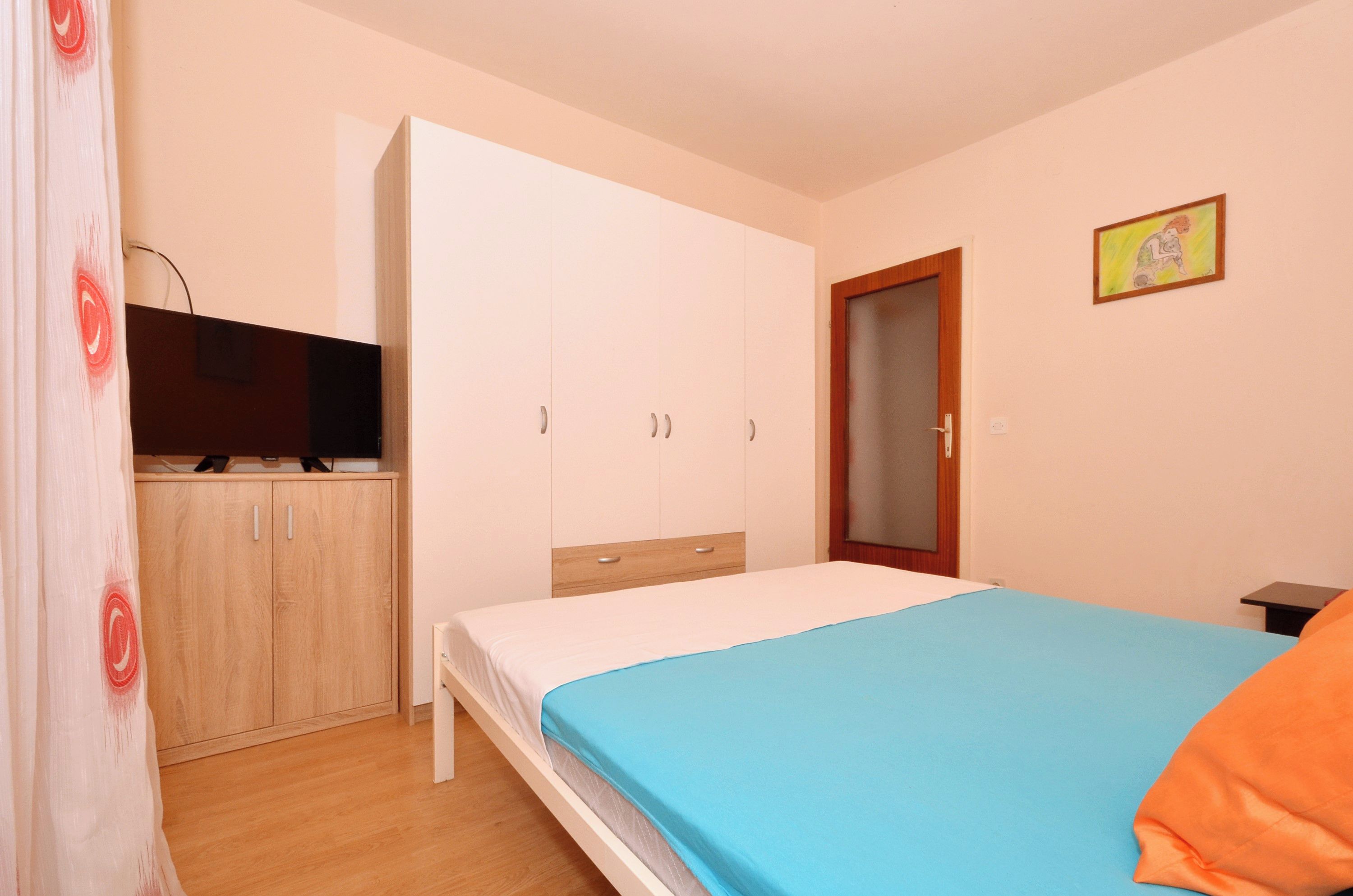 A bedroom with a bed, a wardrobe, a television, and a door.