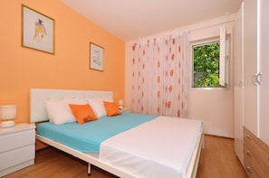 Um quarto com cama, mesas de cabeceira, janela com cortinas e obras de arte nas paredes.