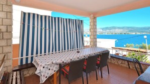 Een balkon met een tafel en stoelen, een gestreept gordijn en uitzicht op zee en bergen.