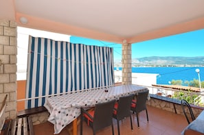 Uma varanda com mesa e cadeiras, uma cortina listrada e vista para o mar e montanhas.
