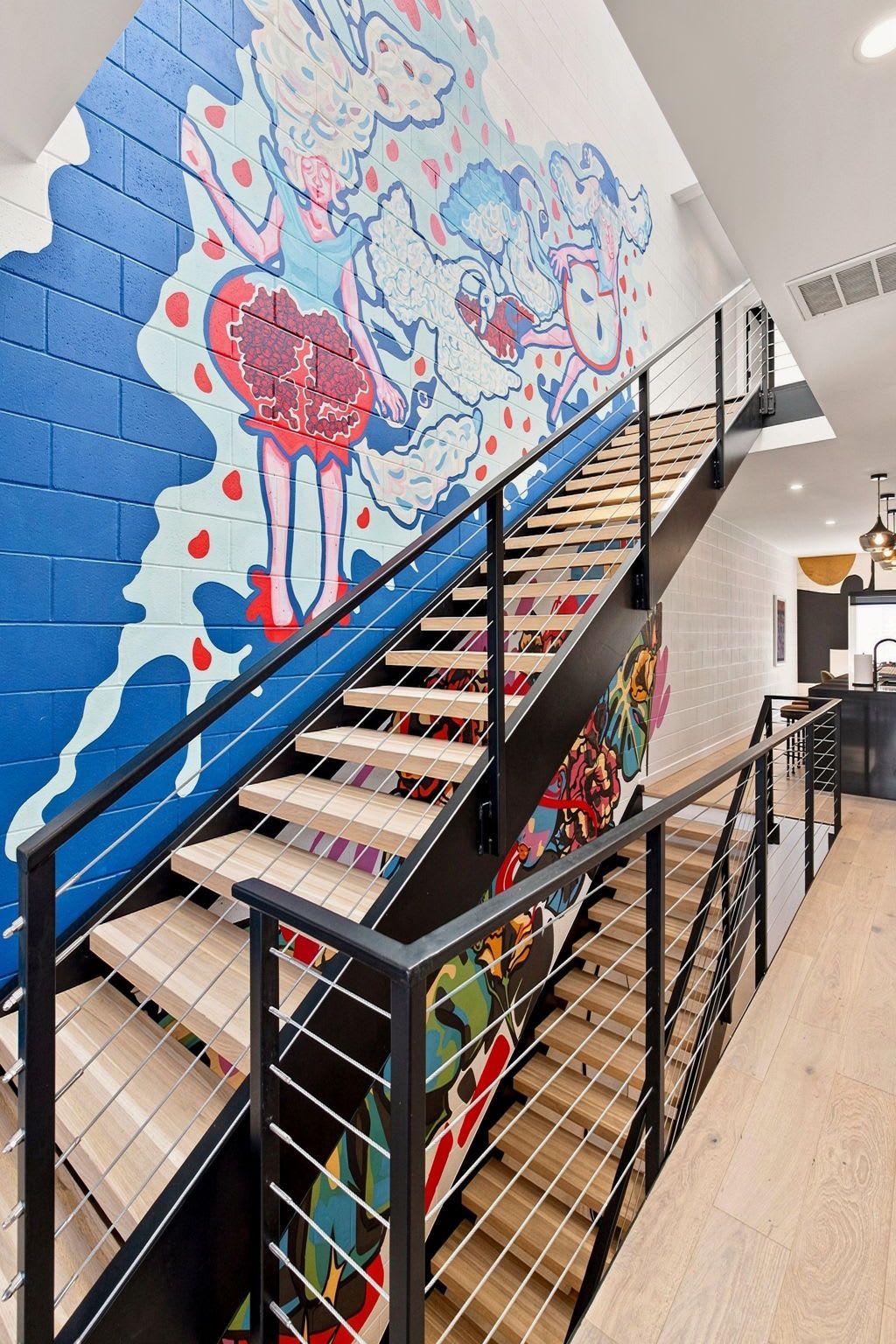 A staircase with a colorful mural on the wall, a wooden floor, and a metal railing.