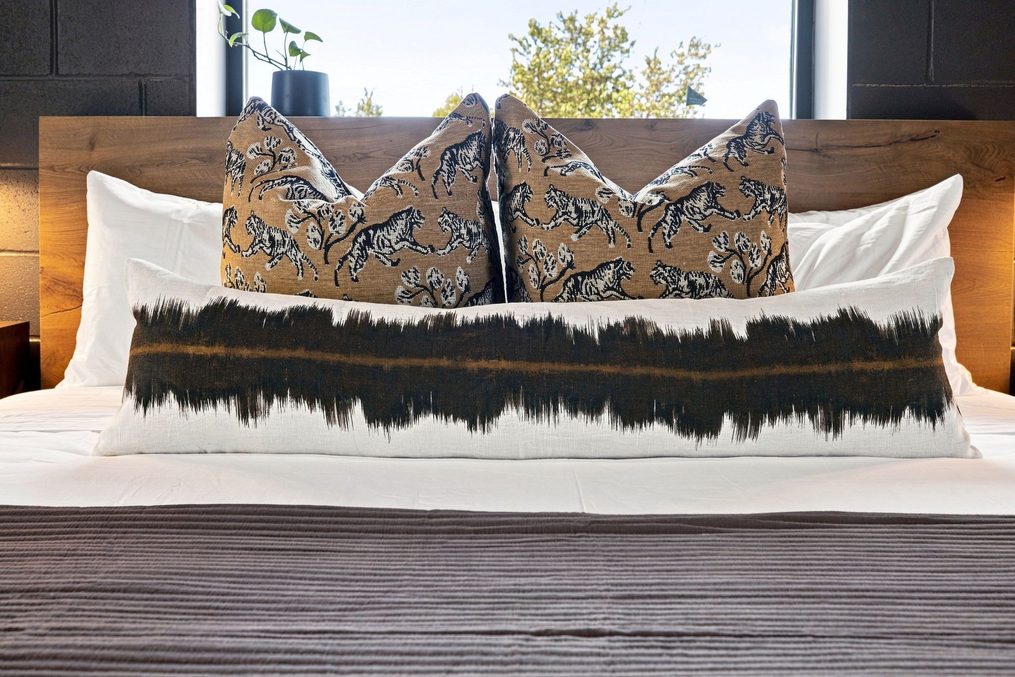 Un lit avec un oreiller à motifs blancs et bruns, un oreiller blanc et un oreiller à motifs de montagnes en noir et brun.