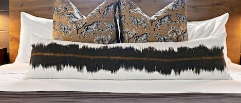 Un lit avec un oreiller à motifs blancs et bruns, un oreiller blanc et un oreiller à motifs de montagnes en noir et brun.