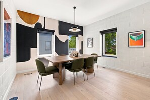 A modern dining room with a wooden table and four chairs, a pendant light, and artwork on the walls. - The Aperture - Garage - 0.5 mi DT (Bentonville)