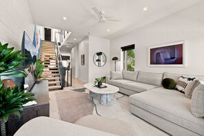 A modern living room with a sofa, coffee table, and a staircase leading to an upper level. - The Aperture - Garage - 0.5 mi DT (Bentonville)