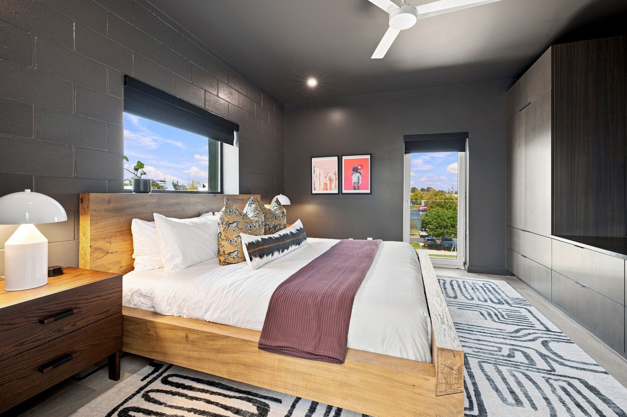 Quarto moderno com cama, mesas de cabeceira, ventilador de teto e vista para o exterior.