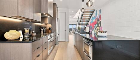 A modern kitchen with dark wood cabinets, stainless steel appliances, and a black countertop.