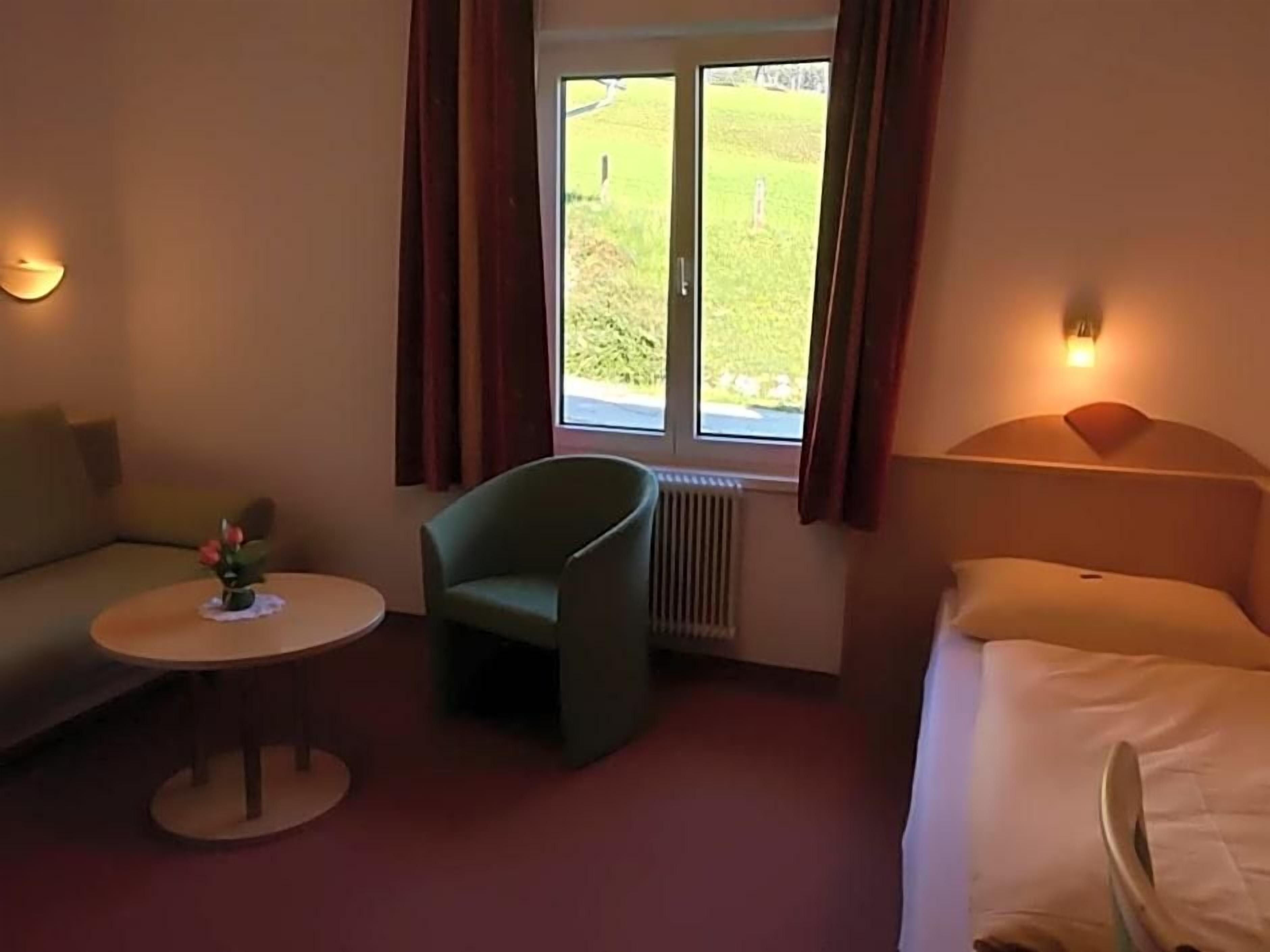 Ein Hotelzimmer mit einem Bett, einem Sofa, einem Sessel, einem kleinen Tisch und einem Fenster mit Vorhängen.