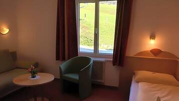 Ein Hotelzimmer mit einem Bett, einem Sofa, einem Sessel, einem kleinen Tisch und einem Fenster mit Vorhängen.