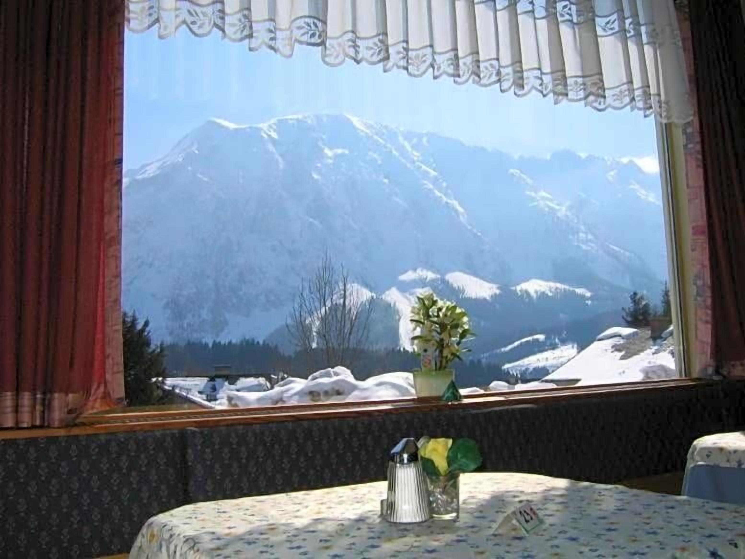Ein Zimmer mit Blick auf schneebedeckte Berge, ein Tisch mit einer blumigen Tischdecke und eine Vase mit Blumen.
