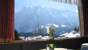 Ein Zimmer mit Blick auf schneebedeckte Berge, ein Tisch mit einer blumigen Tischdecke und eine Vase mit Blumen.