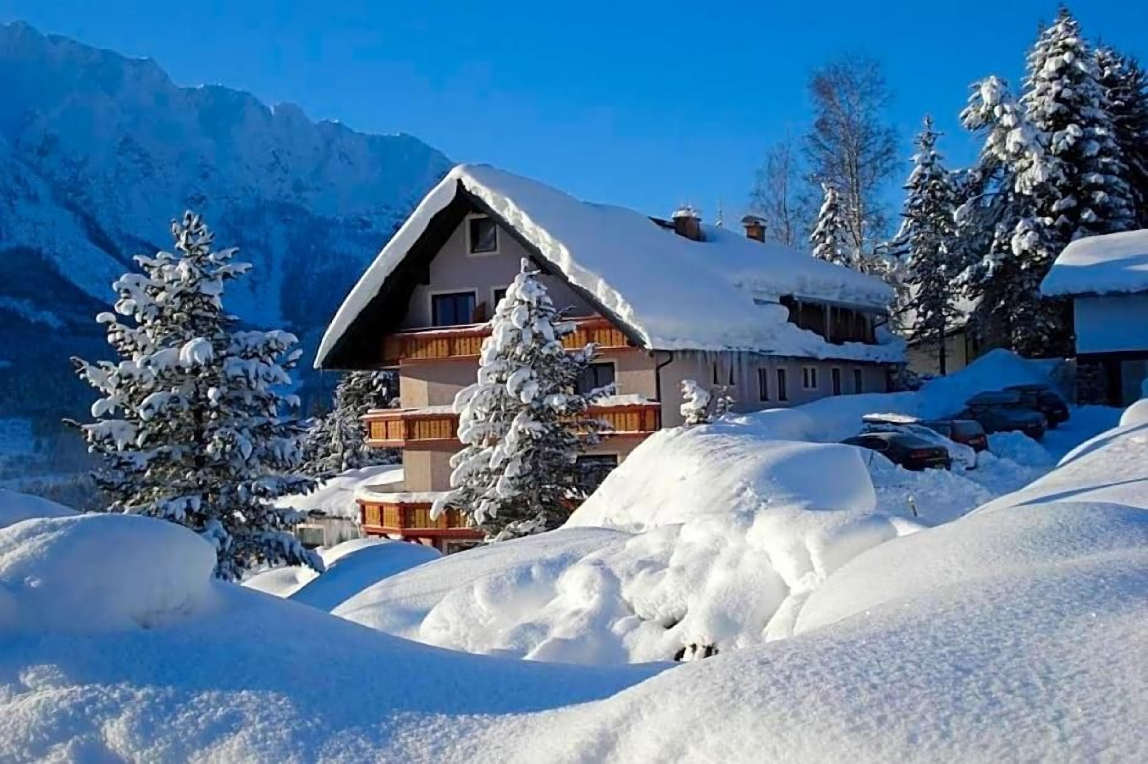Ein Chalet-Hotel mit geneigtem Dach, umgeben von schneebedeckten Bäumen und Bergen.