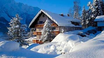 Ein Chalet-Hotel mit geneigtem Dach, umgeben von schneebedeckten Bäumen und Bergen.