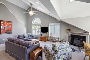 Een ruime woonkamer met een hoge plafond, een open haard, een televisie en een groot raam.