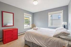 A bedroom with a bed, a red dresser, a mirror, and two windows. - Okemo Winterplace 2BR Loft – Family Ski Getaway (Ludlow)