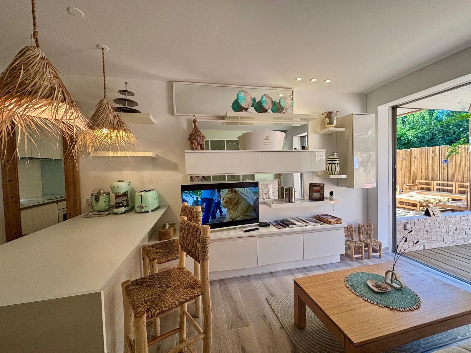 A modern kitchen with a TV, wooden chairs, a dining table, and a view of the outdoors.