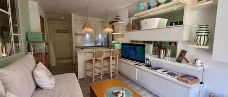 En moderne stue med sofa, sofabord, fjernsyn og et køkkenområde med spiseplads.