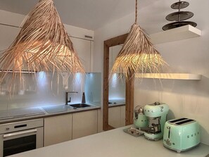 Eine Küche mit modernem Design, ausgestattet mit einer weißen Arbeitsplatte, einem eingebauten Backofen, einer Spüle und einem spiegel mit Holzrahmen. Auf der Arbeitsplatte befinden sich zwei Toaster im Vintage-Stil.