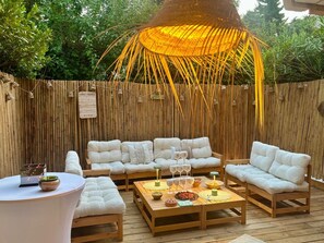 Ein Außenbereich mit Holzterrasse, weißen, gepolsterten Sofas und einer hängenden Leuchte.