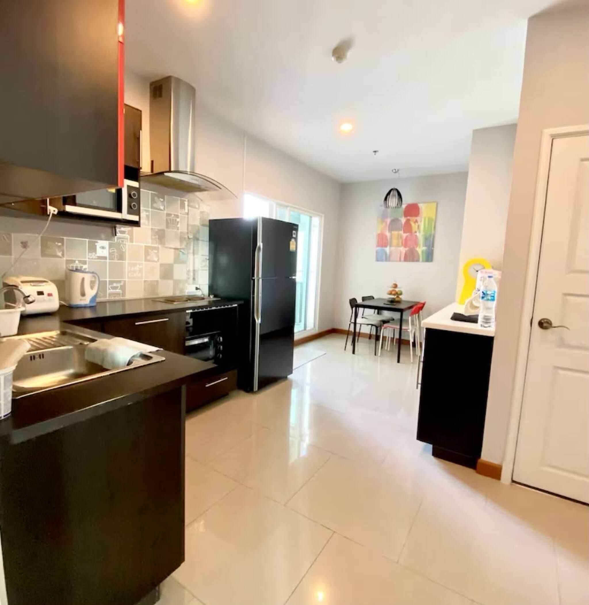 A modern kitchen with a central island, built-in oven, and microwave. There is a dining area with a table and chairs.