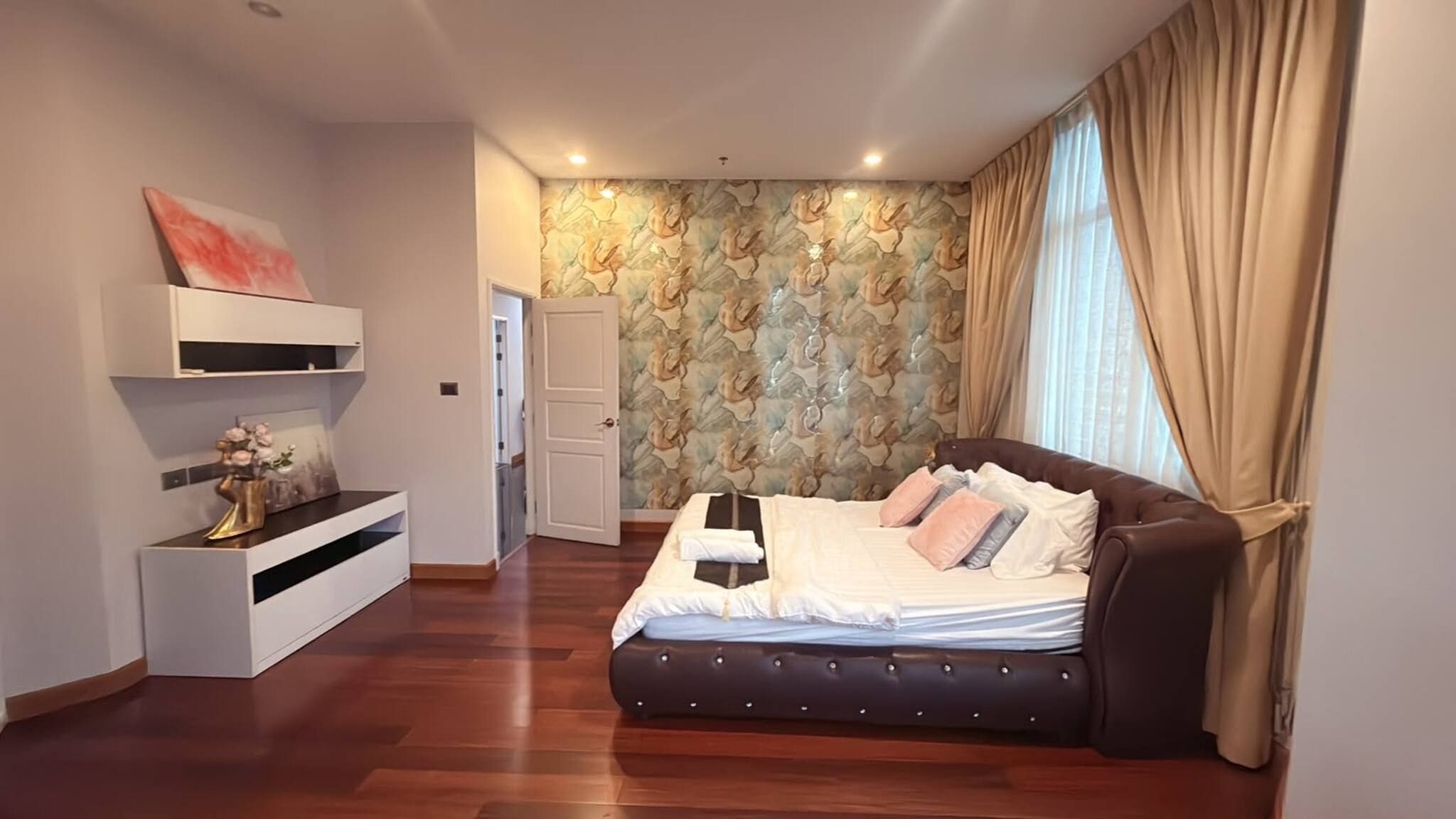 A bedroom with a bed, a wardrobe, a vanity, and a door leading to another room.
