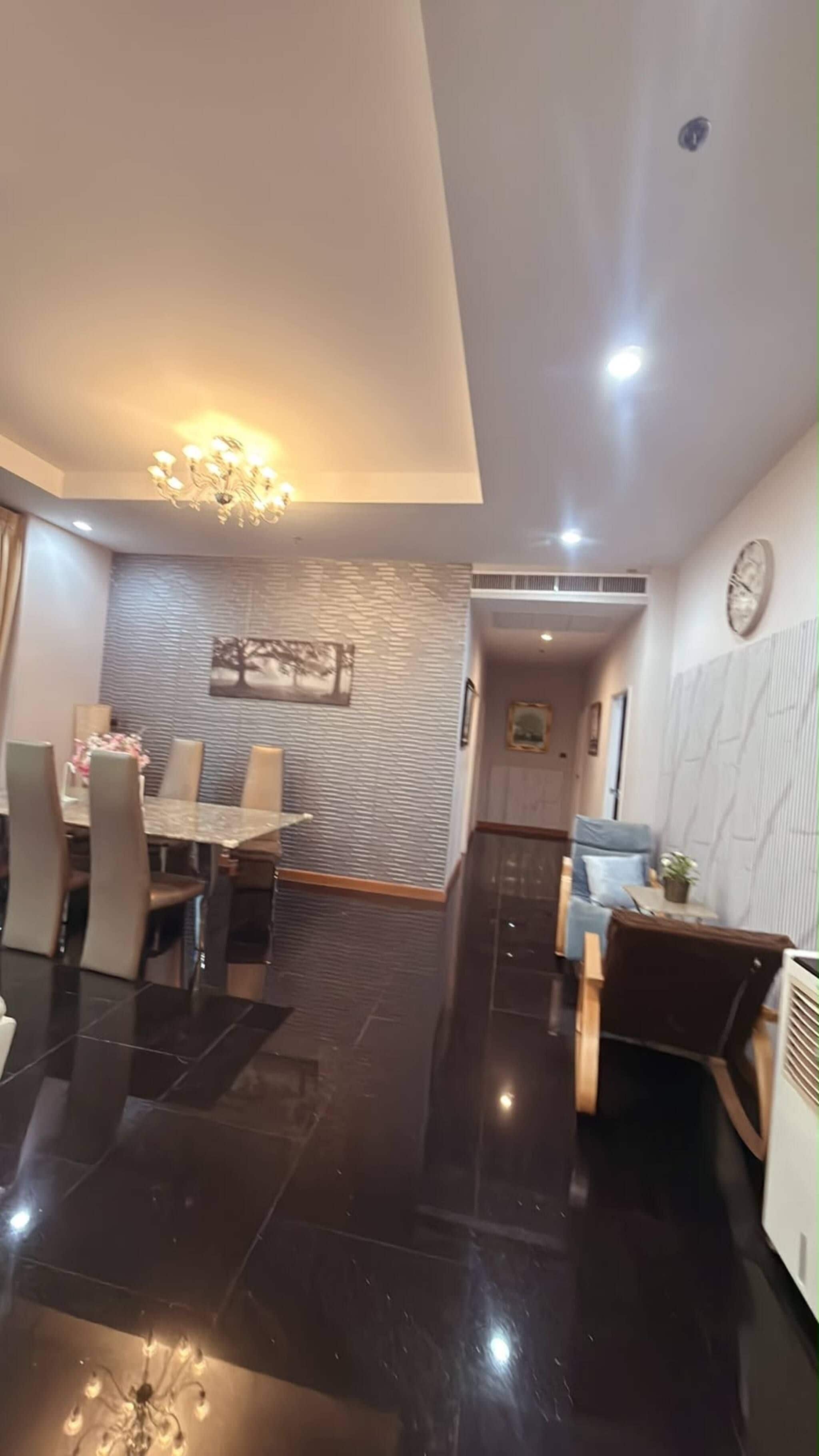 A modern dining area with a chandelier, a dining table with chairs, and a textured wall.