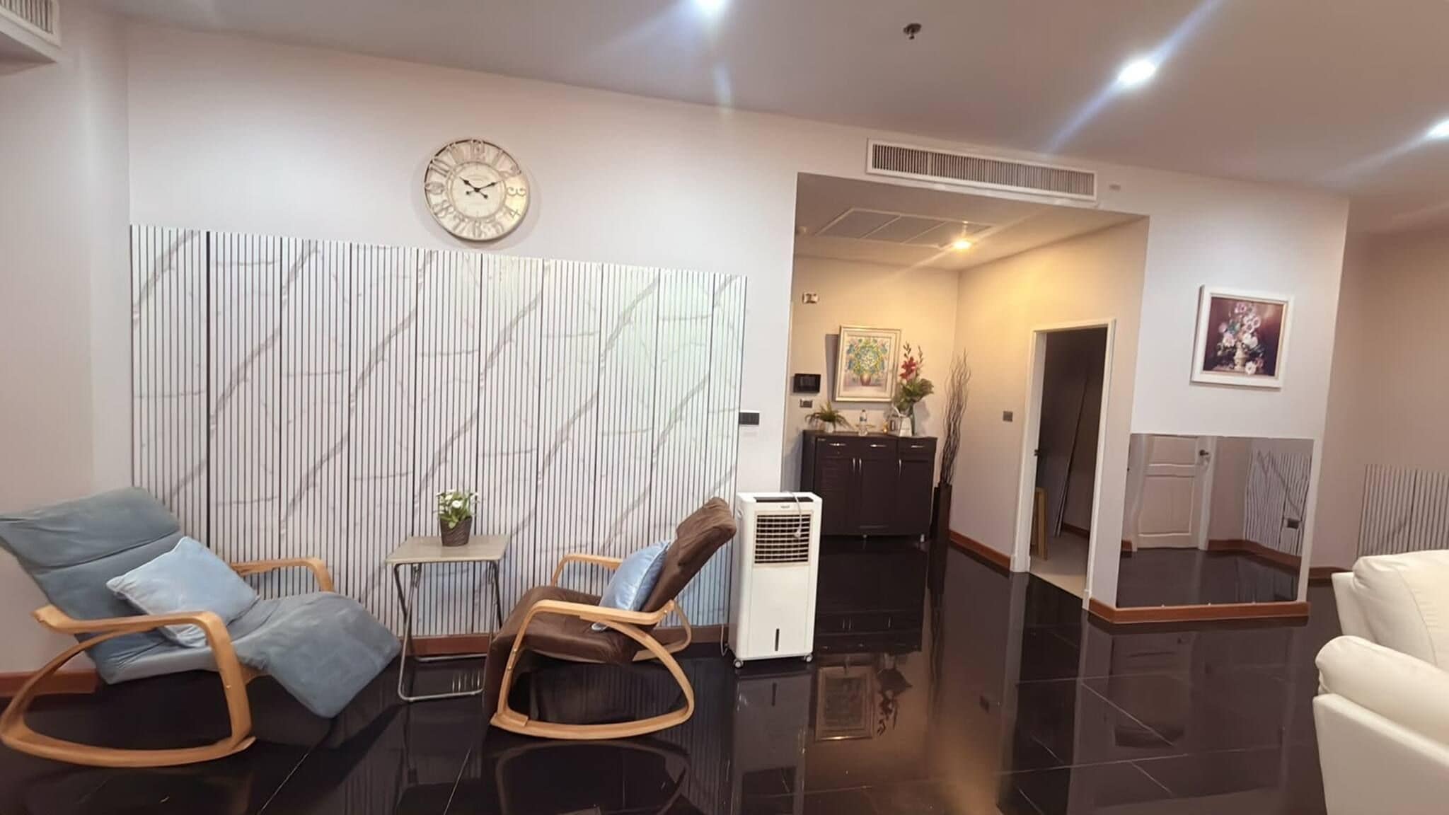A modern living room with a marble-patterned wall, a clock, a small table with a plant, and a seating area with two rocking chairs.