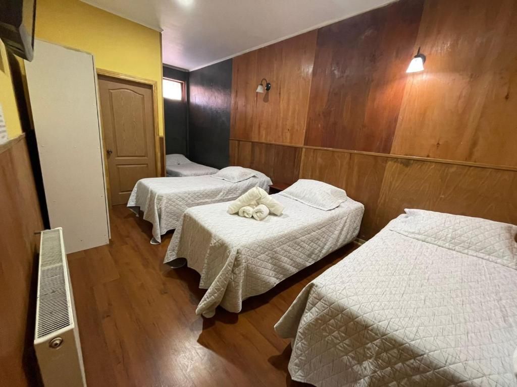 A hotel room with three beds, a wooden wall panel, a white radiator, and a door.