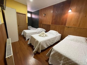 A hotel room with three beds, a wooden wall panel, a white radiator, and a door.