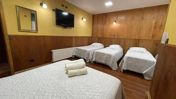 A hotel room with a large bed, two smaller beds, a television, and a mirror on the wall.