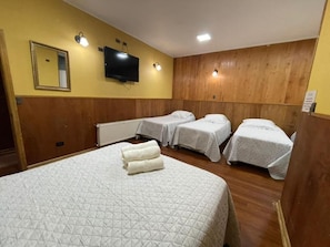 Een hotelkamer met een groot bed, twee kleinere bedden, een televisie en een spiegel aan de muur.