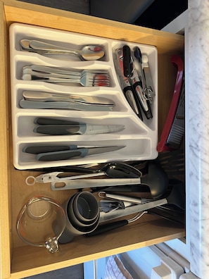 Un cajón con divisiones que contiene varios utensilios de cocina y un recipiente de vidrio.