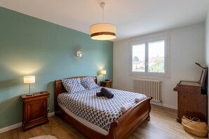 Un dormitorio con una cama de madera, dos lámparas de noche, un radiador, una ventana con vistas y un adorno en la pared.