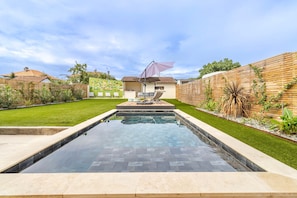Una piscina con solárium, rodeada por un césped cuidado y una valla de madera.