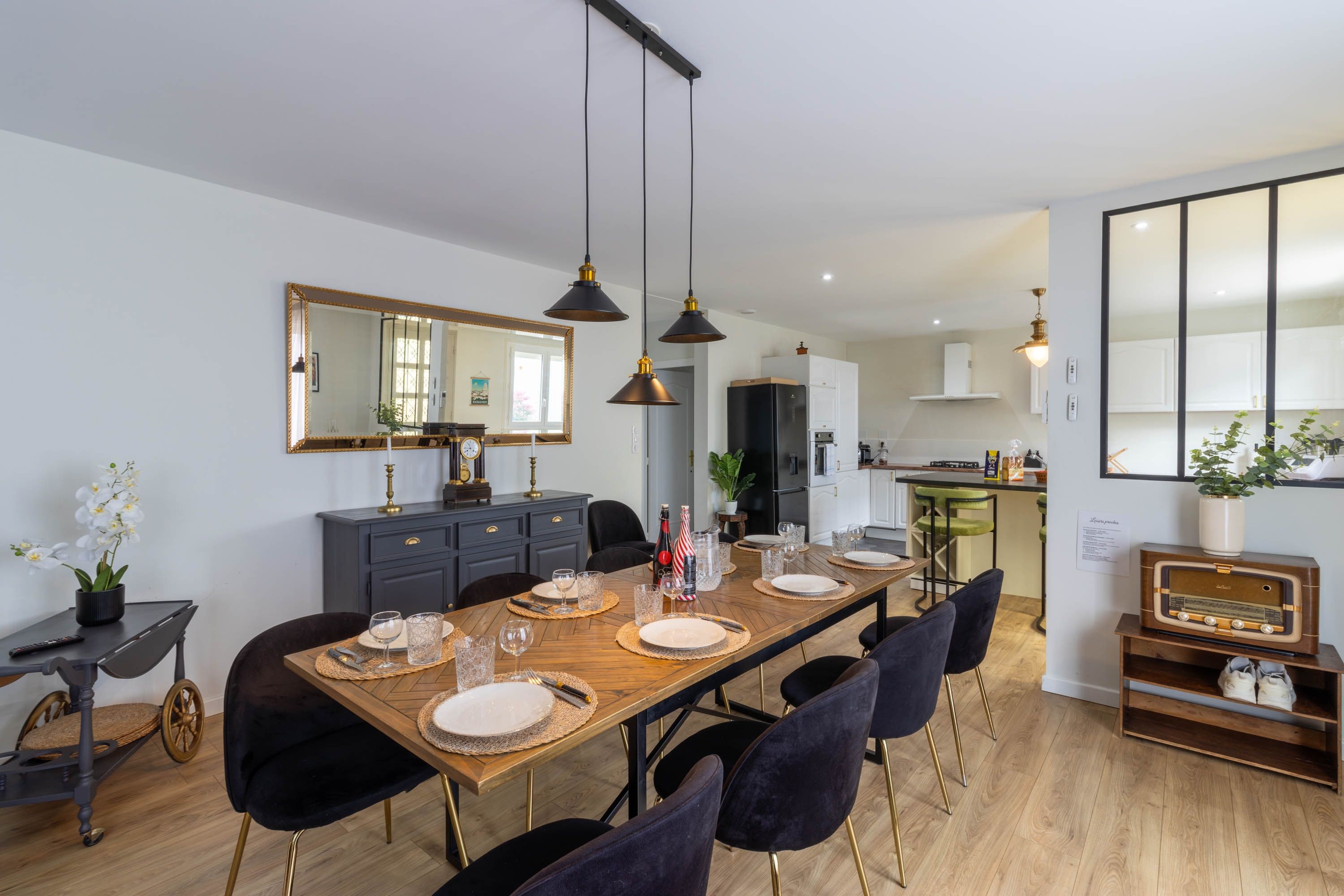 A modern dining area with a wooden table set for four, black chairs, and pendant lighting.